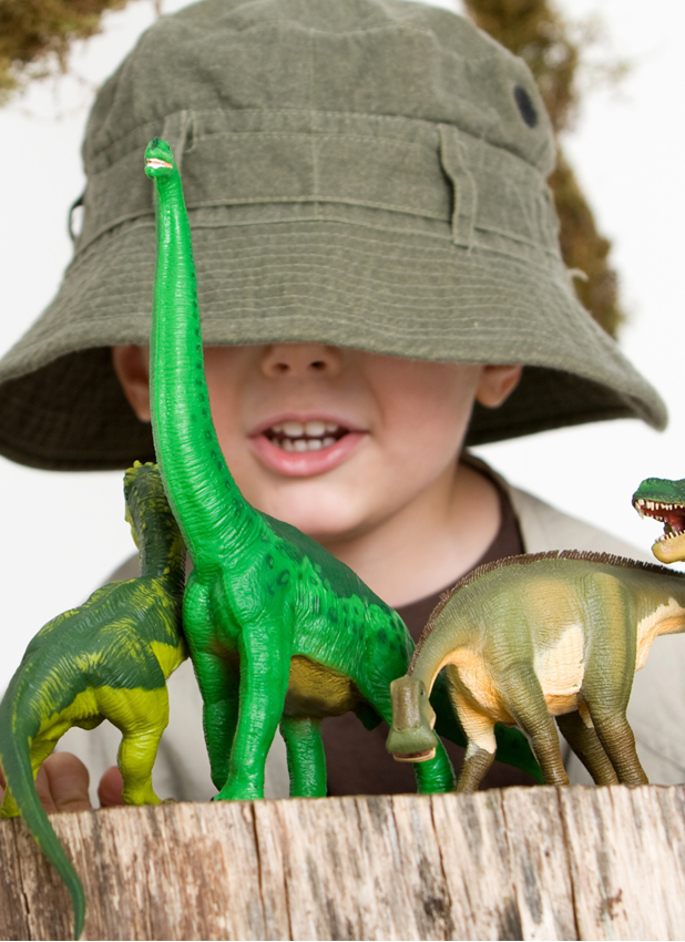 boy in bucket hat behind toy dinosaurs